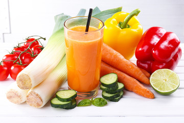 Glass of fresh carrot juice and vegetables on wooden table