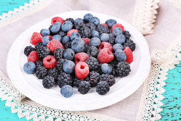 Iced berries on plate, on color wooden background