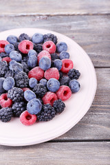 Iced berries on plate, on color wooden background