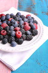 Iced berries on plate, on color wooden background