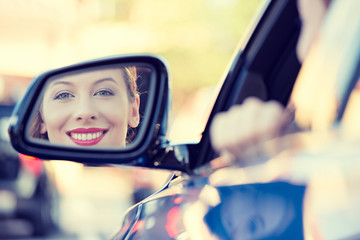 Woman driver looking in car side view mirror smiling