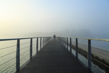 Fototapeta na wymiar Man walking on a footbridge into the morning fog.