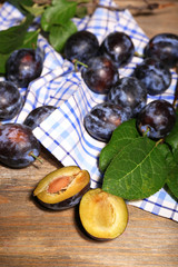 Ripe sweet plums with leaves, on wooden table