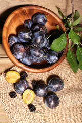 Ripe sweet plums in bowl, on wooden table