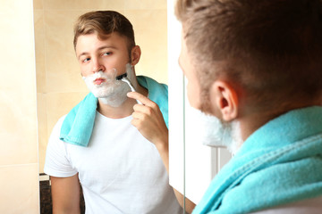 Young man shaving his beard in bathroom