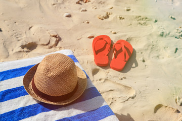 Straw hat, towel and flip flops on a sand beach