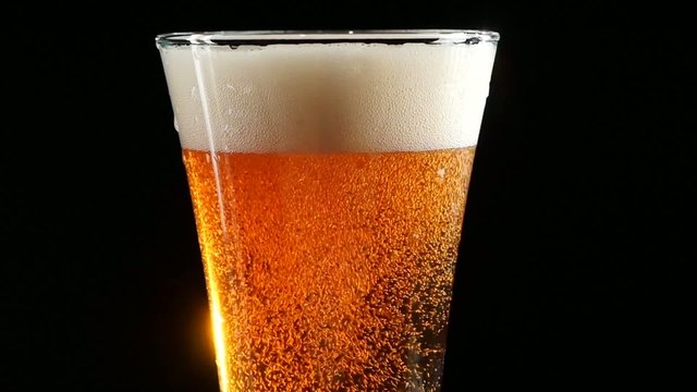 Beer is pouring into a glass on black background. Slow motion.