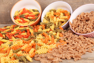 Assortment of colorful pasta in color bowls on wooden
