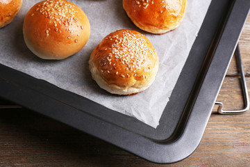 Tasty buns with sesame on oven-tray, on wooden background