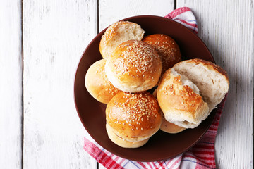 Tasty buns with sesame on plate, on color wooden background