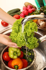 Woman's hands washing vegetables in sink in kitchen
