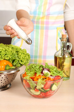 Woman salting vegetable salad in kitchen