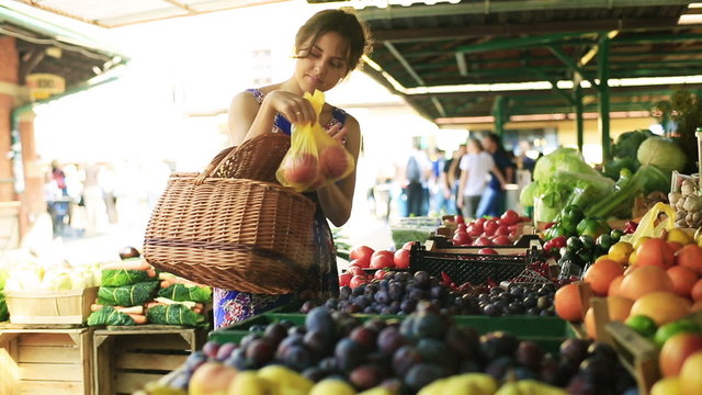 Woman putting tomatoes and peaches to the basket on the market