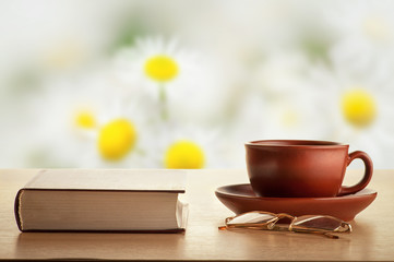 Book, glasses, tea glasses and tea on a background of daisies