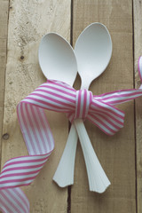 vintage white spoons, pink ribbon on wooden background