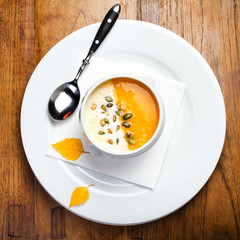 Pumpkin soup with cream and pumpkin seeds in a white bowl on woo
