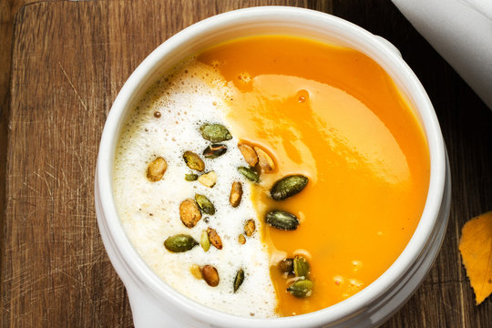 Pumpkin Soup with whipped cream and pumpkin seeds in a white pla