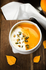 Pumpkin Soup with whipped cream and pumpkin seeds in a white pla