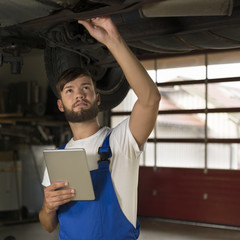 Male car mechanic working under car with tablet PC
