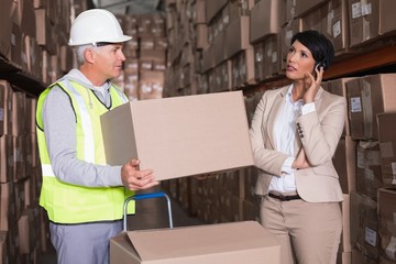 Warehouse worker holding box with manager on a call