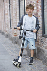 Portrait of young boy with scooter on sidewalk.