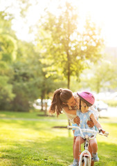 Mother helping baby girl riding bicycle outdoors