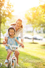 Portrait of happy mother helping baby girl riding bicycle 