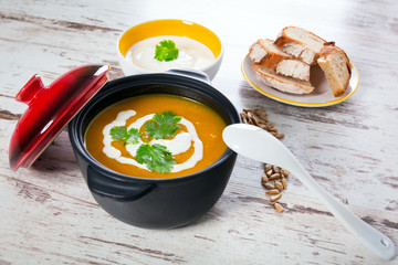 Pumpkin soup with cream in ceramic pot 