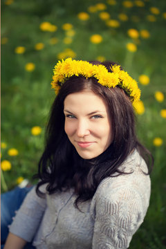 the beautiful girl sits in yellow dandelions with a wreath on th