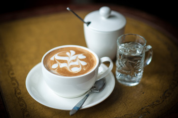 A cup of coffee with flower pattern in a cup on vintage leather