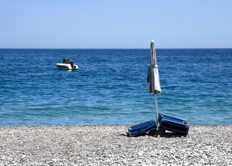 closed beach umbrella and beach chairs on a stony beach