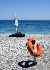 lifebuoy closed beach umbrella and beach chairs on a stony beach