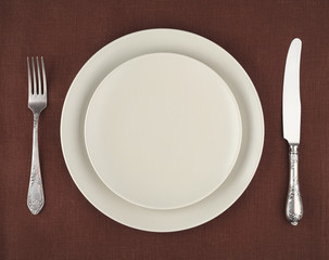 Table setting. Beige plates, fork and knife on brown tablecloth
