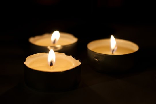Three burning tea lights on black background. Horizontal image