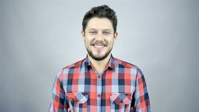 Young smiling man in a red checkered shirt on grey background