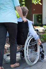 Obraz premium Nurse walking with elderly woman on wheelchair