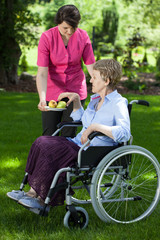 Caregiver giving pear to disabled senior woman