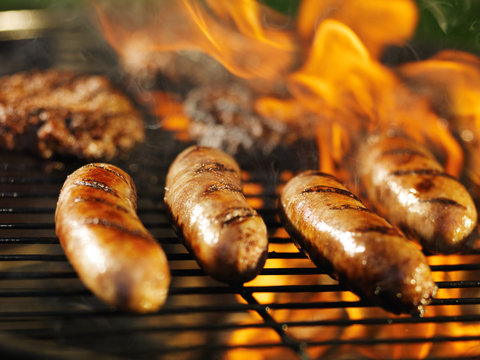 bratwursts cooking on flaming grill