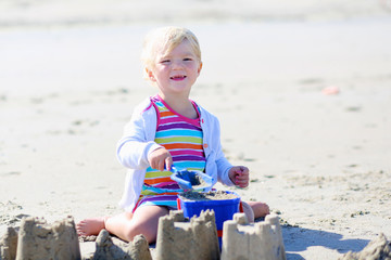 Little happy girl building sand castles on the beach