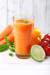 Glass of fresh carrot juice and vegetables on wooden table