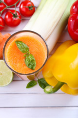 Glass of fresh carrot juice and vegetables on wooden background