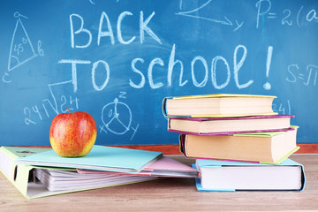 School supplies on table on blackboard background