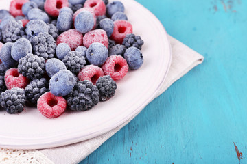 Iced berries on plate, on color wooden background