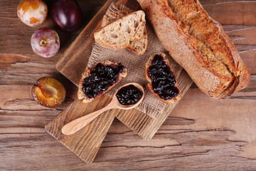 Bread with plum jam and plums on wooden table close-up