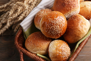 Tasty buns with sesame in wicker basket, on  wooden background