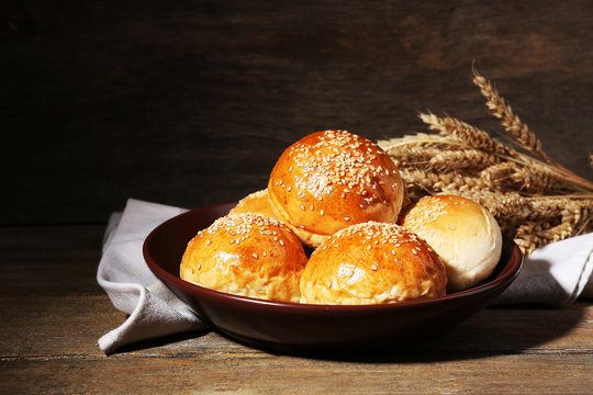 Tasty buns with sesame on plate, on wooden background