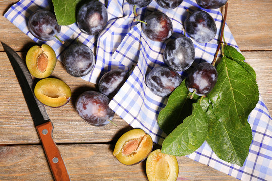 Ripe sweet plums with leaves, on wooden table