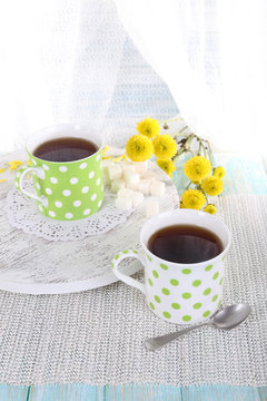 Two polka dot cups of tea on table on curtain background
