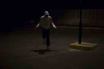 Fototapeta na wymiar Hooded man skipping at night under a street light