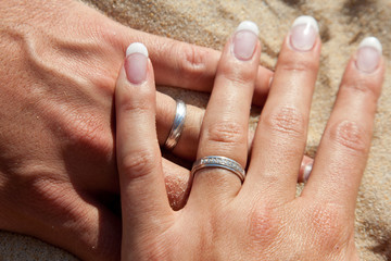 Jolies mains des mariés dans le sable avec les alliances du mariage
